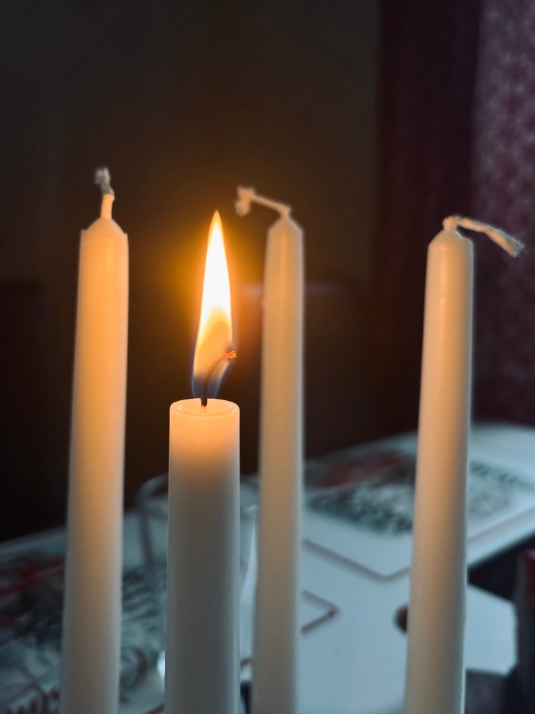 Bilden visar fyra vita, varav ett är tänt. Lågan är klart gul-orange och fokus ligger på veken som brinner. De andra tre ljuden är .